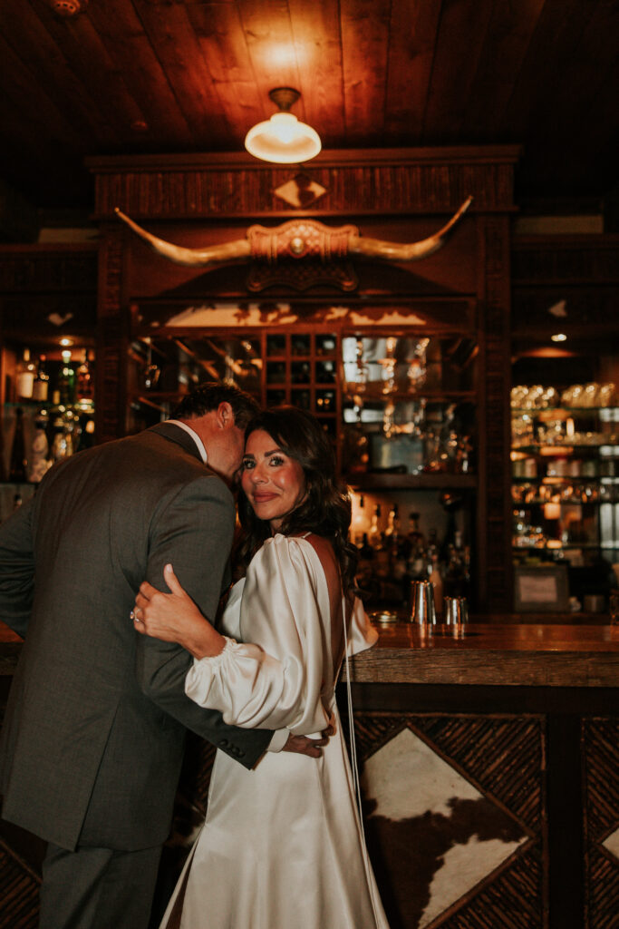 Bride smiling while snuggled into groom inside bar