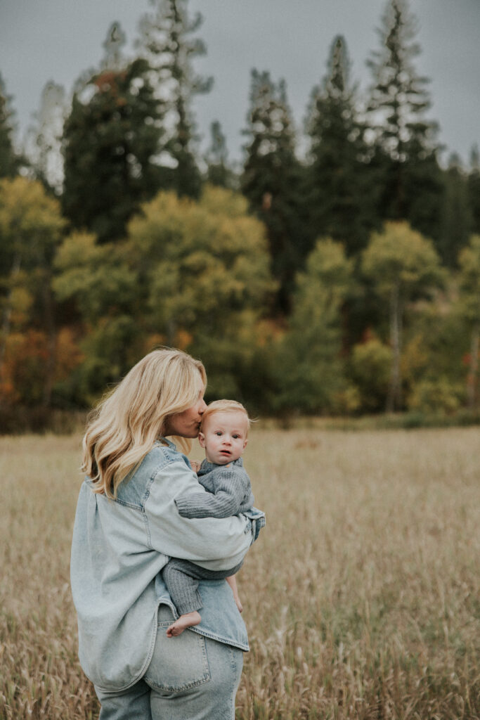 Mother holding her baby in a Montana field surrounded by fall trees